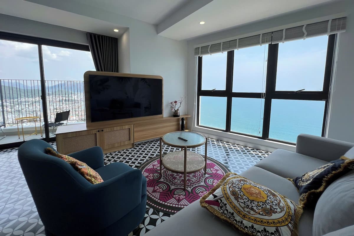 Ein modernes Wohnzimmer mit großem Fernseher, bequemen Sitzmöglichkeiten, einem kleinen runden Tisch und einem Balkon mit Meerblick.