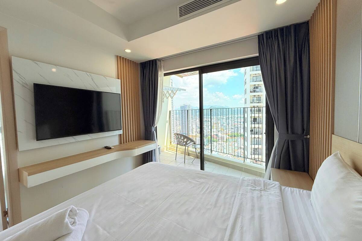 Ein Hotelzimmer mit einem großen Bett, einem flachbildfernseher an der Wand, einem Balkon mit Blick auf die Stadt und einer Schiebetür.