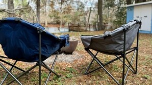 Zwei Campingstühle in einer Naturkulisse mit Bäumen und einem Gebäude im Hintergrund.