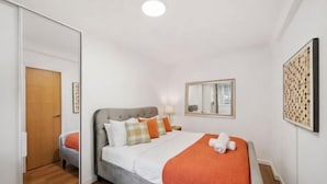 A bedroom with a bed, a mirror, a wall art piece, and a wooden door. - Sherborne Court Residences (London)