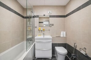 A bathroom with a glass shower enclosure, a white sink, and a toilet. - Sherborne Court Residences (London)