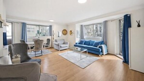 A modern living room with a blue sofa, a glass coffee table, and a dining area with a white table and chairs. - Sherborne Court Residences (London)