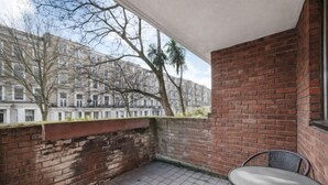 A small balcony with a tiled floor, a brick wall, and a view of a building with trees. - Sherborne Court Residences (London)