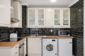 A compact kitchen with white cabinets, a microwave, a washing machine, and a toaster. - Sherborne Court Residences (London)