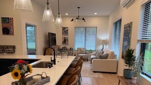 A modern kitchen with a central island, dining chairs, pendant lights, and a view of the living area with a sofa and a potted plant. - Tranquil 1 bedroom in-law suite - walking distance to downtown Delafield (Delafield)