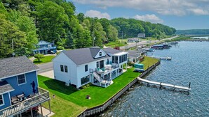 En fastighet vid vattnet med ett stort hus som har en veranda och en brygga som sträcker sig ut i vattnet.