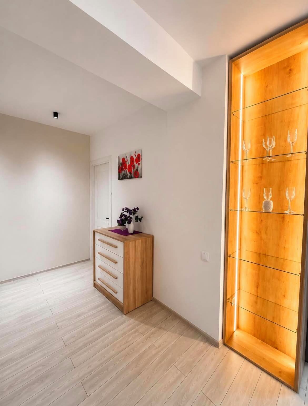 Een kamer met een houten kast, een kunstwerk aan de muur, en een kast met wijnglazen.