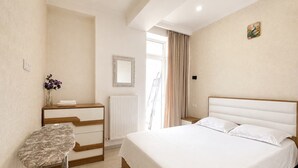 Quarto com cama, cômoda, espelho, radiador e janela com cortinas.