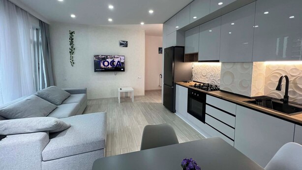 Ein modernes Wohnzimmer mit einem grauen Sofa, einem kleinen weißen Tisch und einem an der Wand befestigten Fernseher.