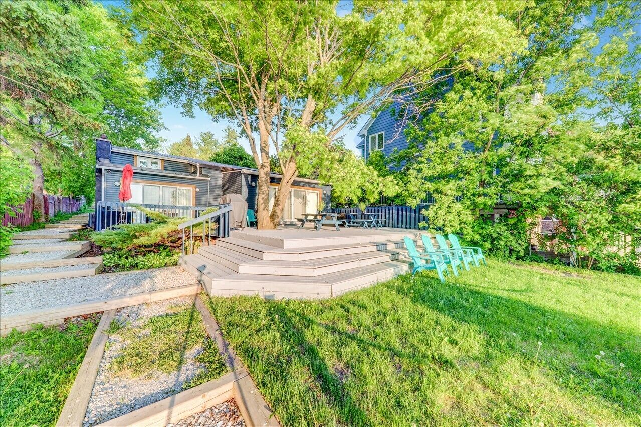 A modern house with a deck, surrounded by lush greenery and a blue fence.
