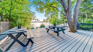 Une terrasse en bois, agrémentée de tables de pique-nique et de plantes en pot, donnant sur une étendue d’eau.