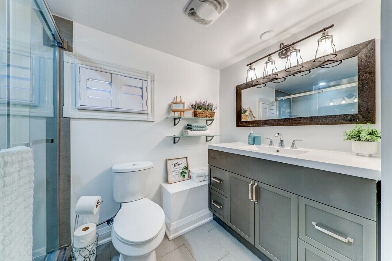Ein modernes Badezimmer mit Toilette in Weiß, einem großen Spiegel mit Holzrahmen und einem weißen Waschbecken mit dunklem Unterschrank.