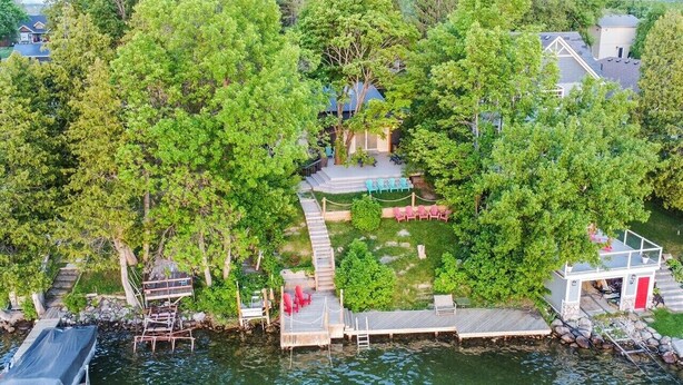 Vue aérienne d’une propriété au bord du lac, avec un quai, un petit bâtiment et une terrasse équipée de chaises.