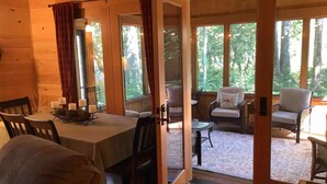 L’intérieur chaleureux d’un chalet comprend un coin repas, un espace salon avec vue sur la forêt et une porte donnant sur l’extérieur.