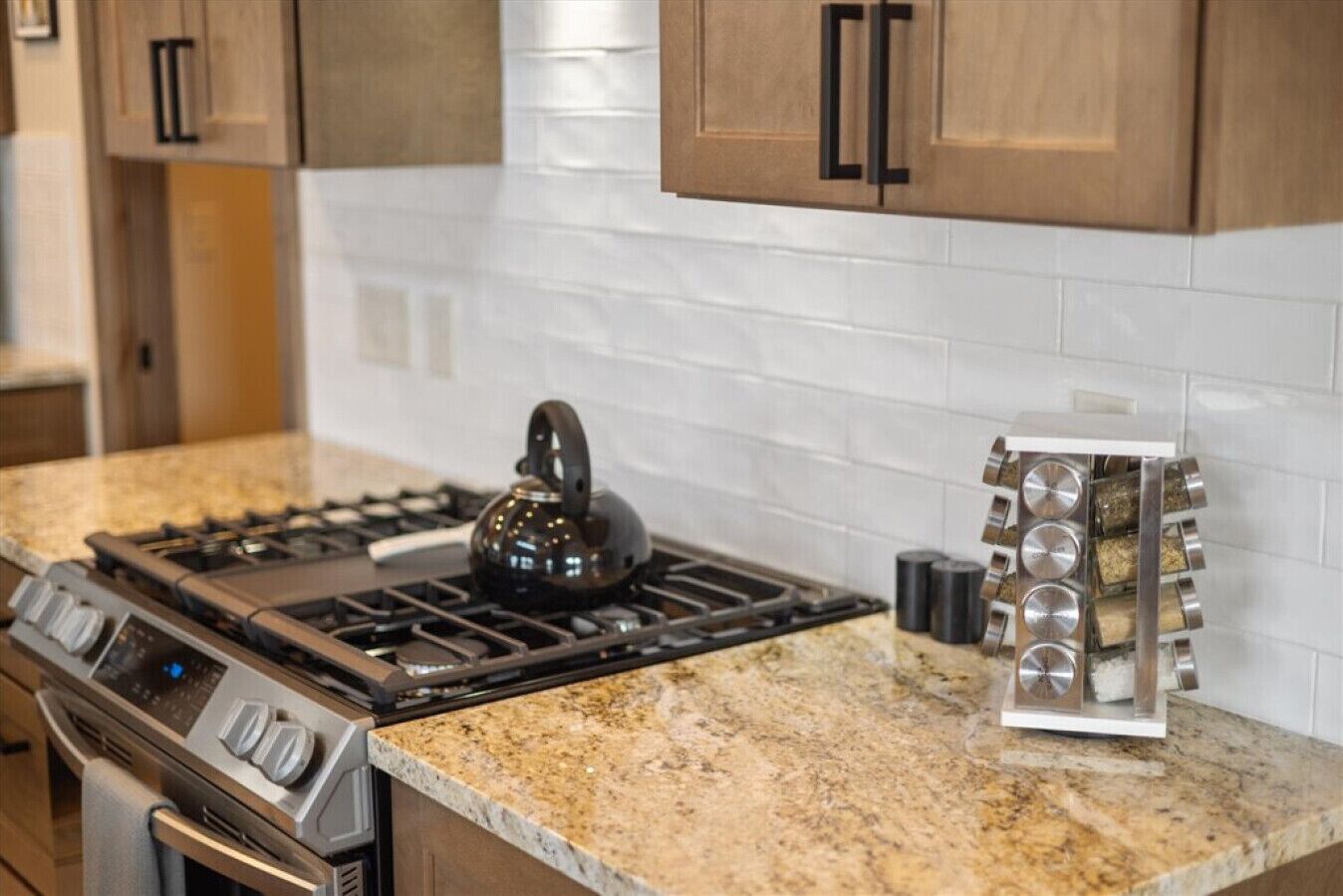 A kitchen with a gas stove, a kettle, and a spice rack.