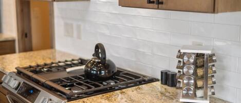 A kitchen with a gas stove, a kettle, and a spice rack.