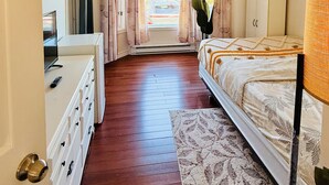 Une chambre à coucher avec un lit, une commode, un téléviseur, une fenêtre avec des rideaux et une vue sur l’extérieur.
