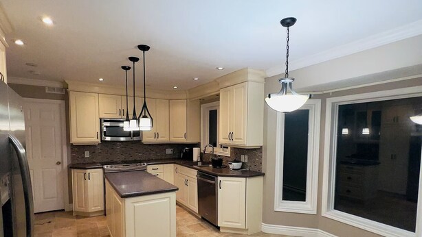 Une cuisine moderne dotée d’un îlot central, de luminaires suspendus et d’une grande fenêtre offrant une vue dégagée.