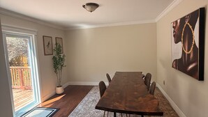Un vaste espace dédié à la salle à manger, avec une grande table en bois, un tapis à motifs et une vue sur une terrasse en bois, accessible par une porte vitrée.