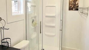 Une salle de bain avec une douche à parois de verre, des toilettes, un lavabo et une fenêtre.