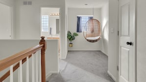 A hallway with a wooden railing, a hanging chair, a potted plant, and a door with a light switch. - Modern Luxury Home near Denver (Westminster)
