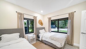 Een moderne slaapkamer met twee bedden, een nachtkastje en een groot raam.