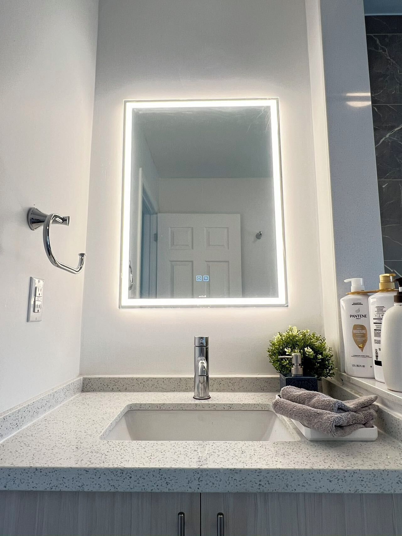 Een badkamer met een wit wastafel, een spiegel met verlichting, een handdoek en toiletartikelen op de aanrecht.
