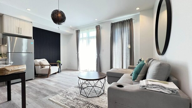 A modern living room with a sofa, a dining table, and a kitchen area with a refrigerator. - Bentley Commons Luxury 4 Bedroom Townhome in the Fallsview Tourist District (Niagara Falls)