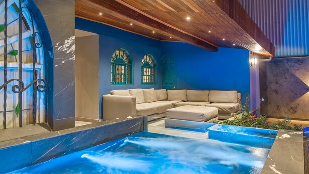 Área de spa com hidromassagem, sofá bege e janelas decorativas.