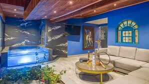 Uma sala de estar moderna com parede azul, mesa de centro redonda de vidro, sofá bege, TV na parede e um narguilé decorativo.