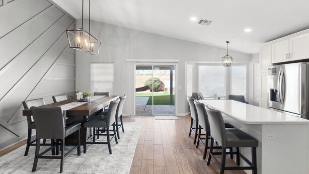 Una cocina moderna con una isla central, armarios blancos y un comedor con mesa y sillas de madera.