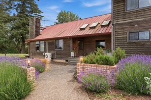 A wooden house with a red roof, a brick pathway, and lavender plants.