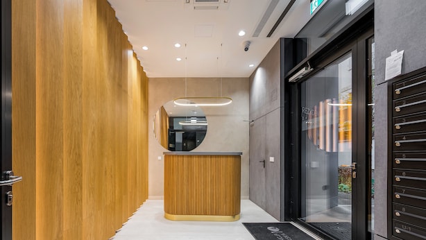 A modern reception area with a wooden reception desk, a glass door leading to a room, and a digital display above the desk.