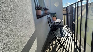 Un balcon avec une petite table et des chaises, des plantes en pot et une vue sur le paysage urbain.