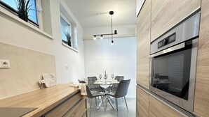 Une cuisine moderne avec des meubles en bois, un four encastré et un coin repas comprenant une table et des chaises en verre.