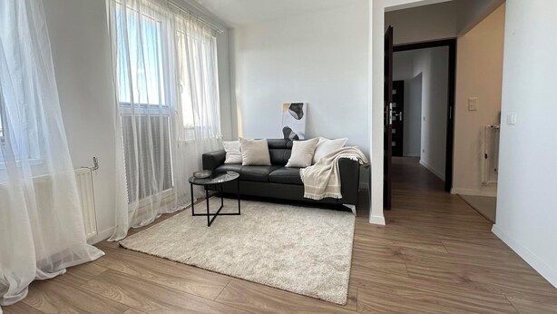 Un salon moderne avec un canapé en cuir noir, une petite table ronde et un tapis beige.