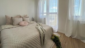 Une chambre avec un grand lit, des rideaux blancs et une vue sur l’extérieur.