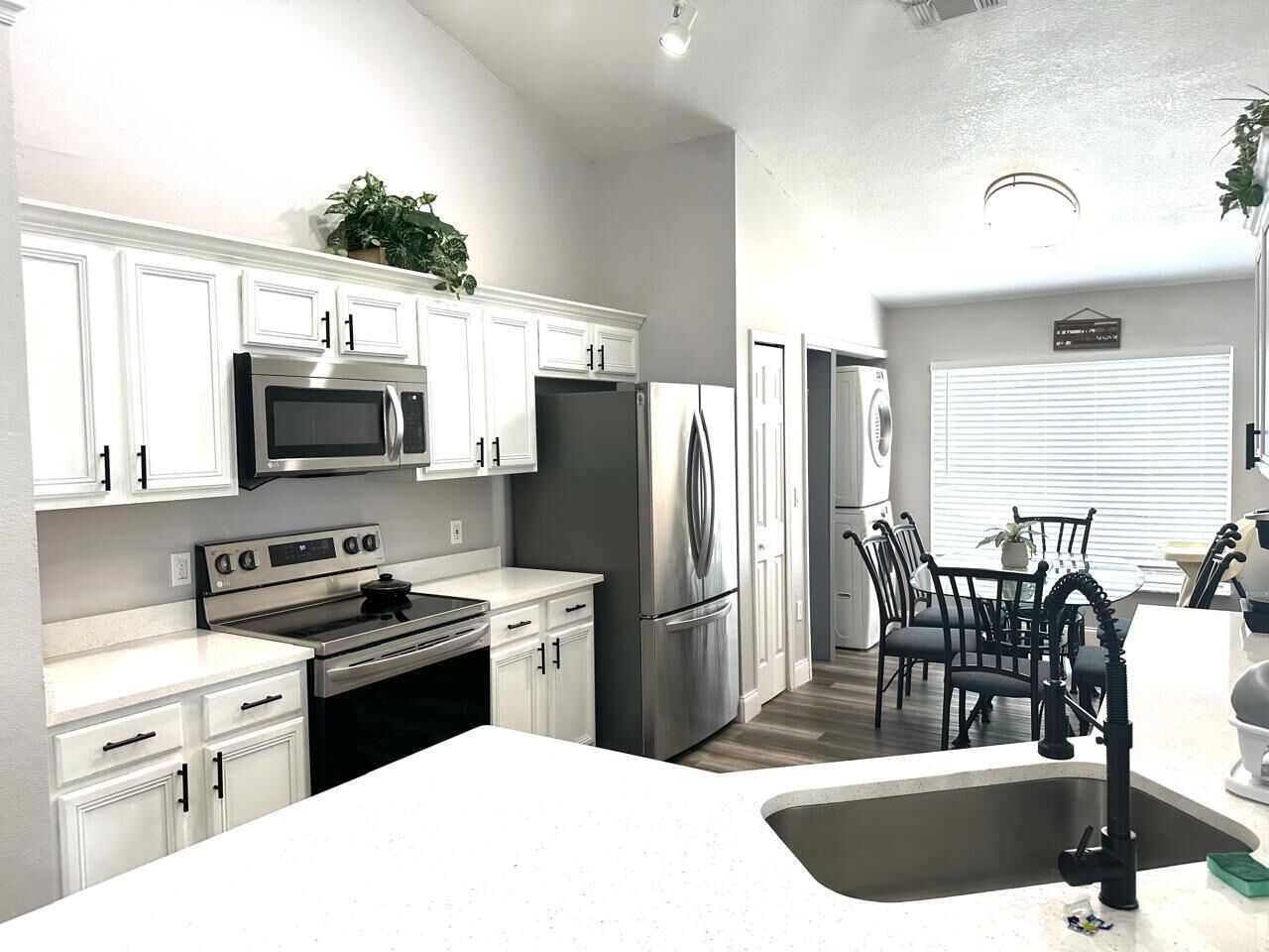A modern kitchen with white cabinetry, stainless steel appliances, and a dining area with black chairs and a table.