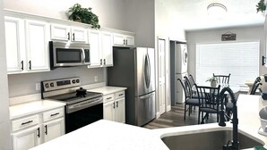 Une cuisine moderne avec des meubles blancs, des appareils en acier inoxydable et un coin repas doté de chaises et d’une table noires.