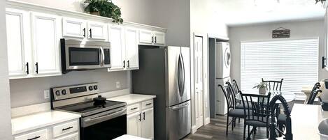 A modern kitchen with white cabinetry, stainless steel appliances, and a dining area with black chairs and a table.