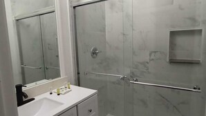 Une salle de bain moderne avec une douche à l’italienne en verre, un meuble-lavabo blanc et un grand miroir.