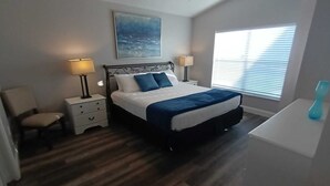 Une chambre à coucher avec un lit, des tables de chevet, une chaise, une fenêtre avec des stores et un tableau au mur.