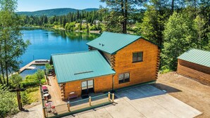 A log cabin with a green roof, a dock, and a view of a lake surrounded by trees. - Cozy 4-bedroom waterfront Cabin in peaceful Ione with AC. Sleeps 14! (Ione)