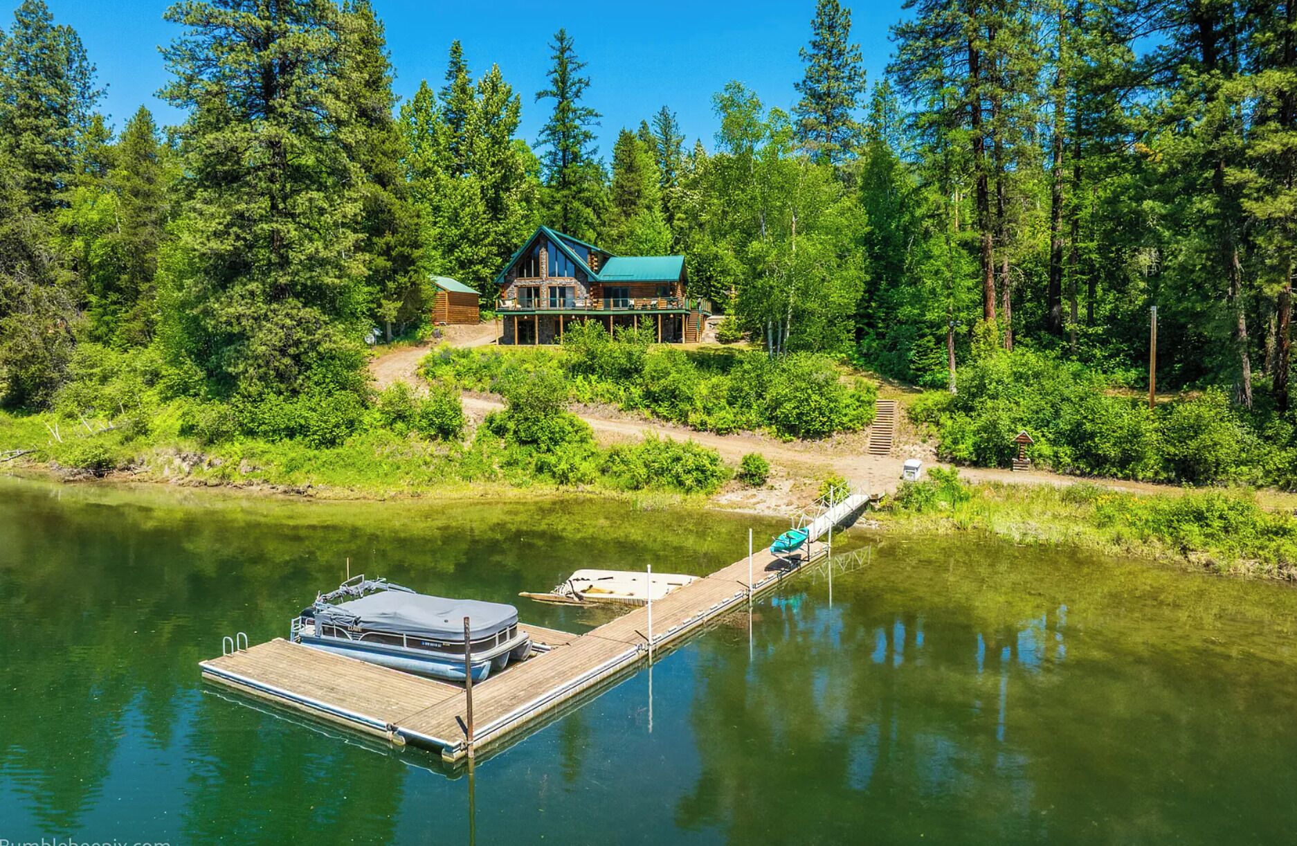 Une cabane avec un quai s’avançant dans un lac paisible, entourée d’une forêt dense.