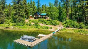 Une cabane avec un quai s’avançant dans un lac paisible, entourée d’une forêt dense.
