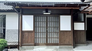 Une maison traditionnelle japonaise avec une porte d’entrée en bois, un dallage en pierre et un toit recouvert de tuiles.