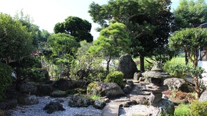 Un jardin japonais traditionnel, avec des allées pavées de pierres, des rochers et divers arbres.