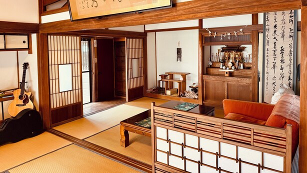Une pièce de style japonais traditionnel, avec un sol recouvert de tatamis, une petite table en bois, un canapé et une guitare.