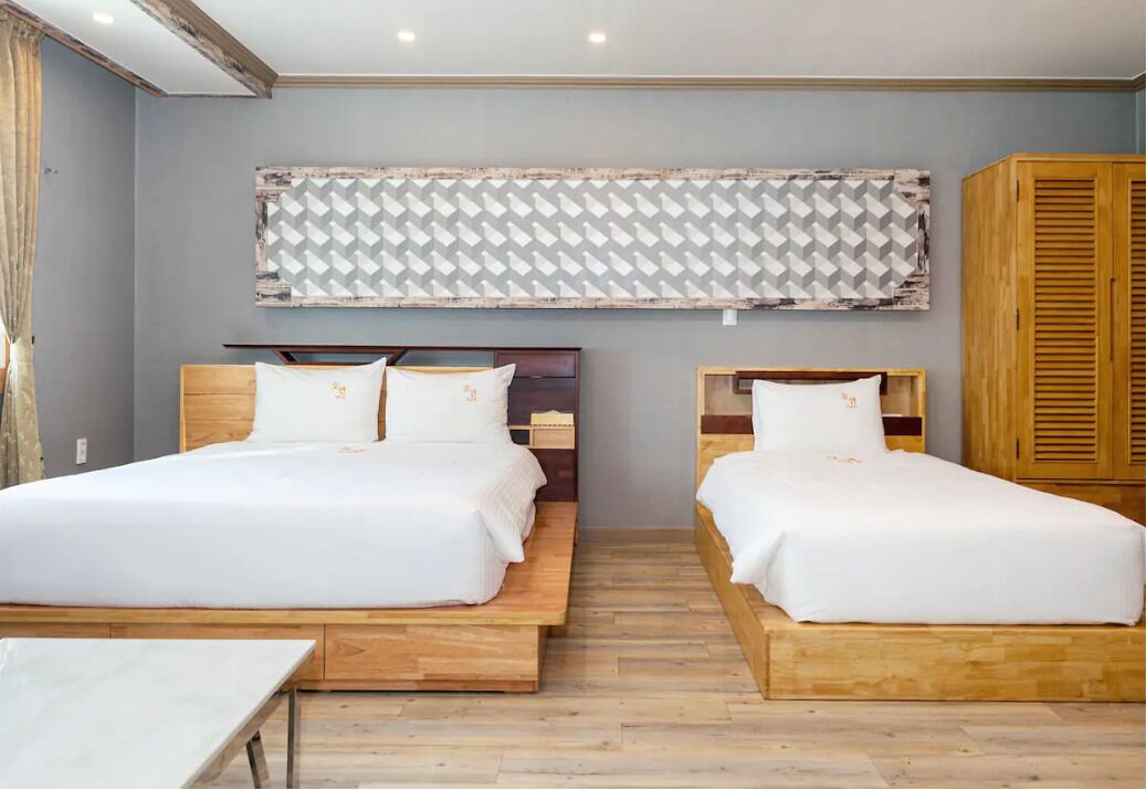 A room with two beds, wooden headboards, a large patterned curtain, and a wooden wardrobe.