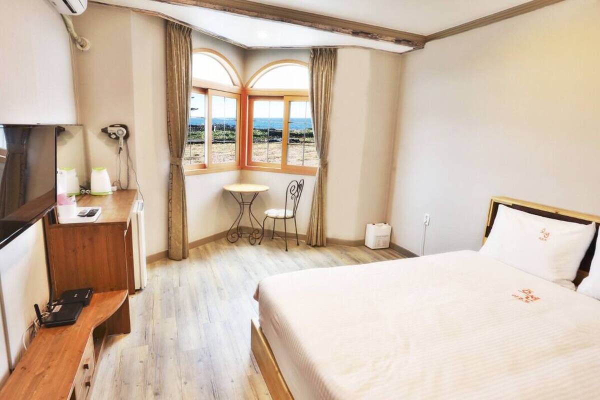 A hotel room with a large bed, a desk with a chair, a small table, and a window with curtains.